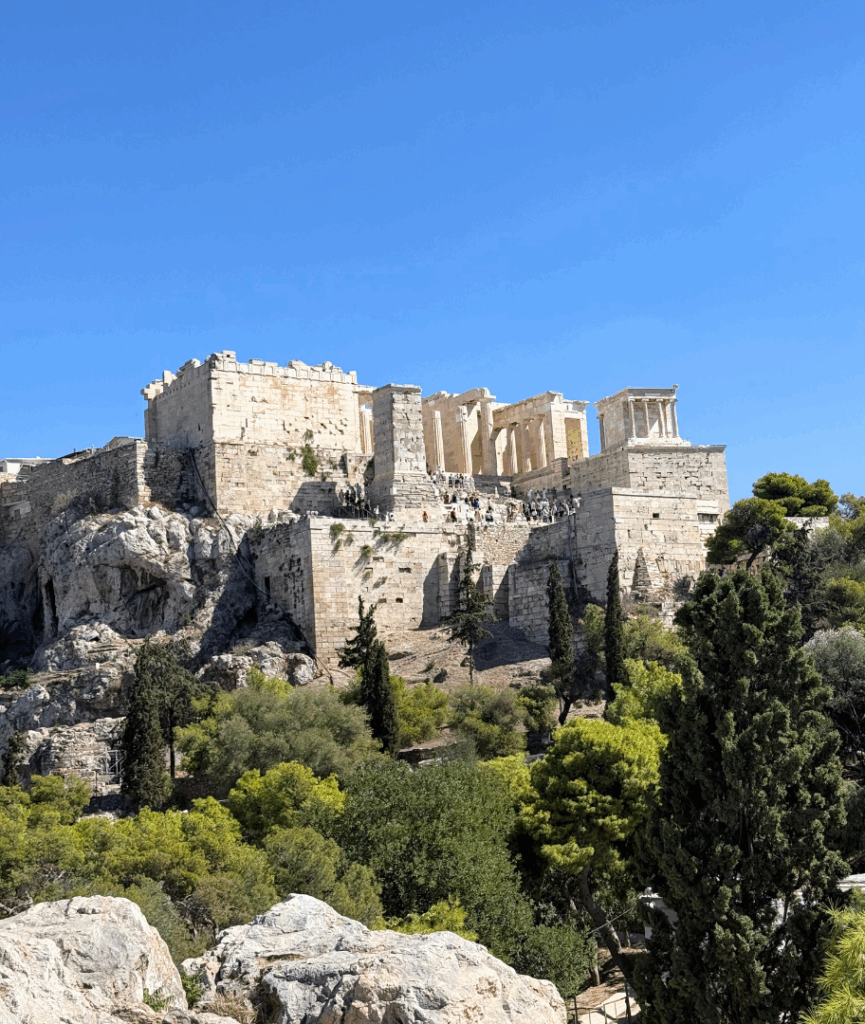Distant view of the Acropolis on a rocky hill under a clear blue sky—ancient stone temples surrounded by trees; a metaphor for enduring monuments vs. evolving websites.